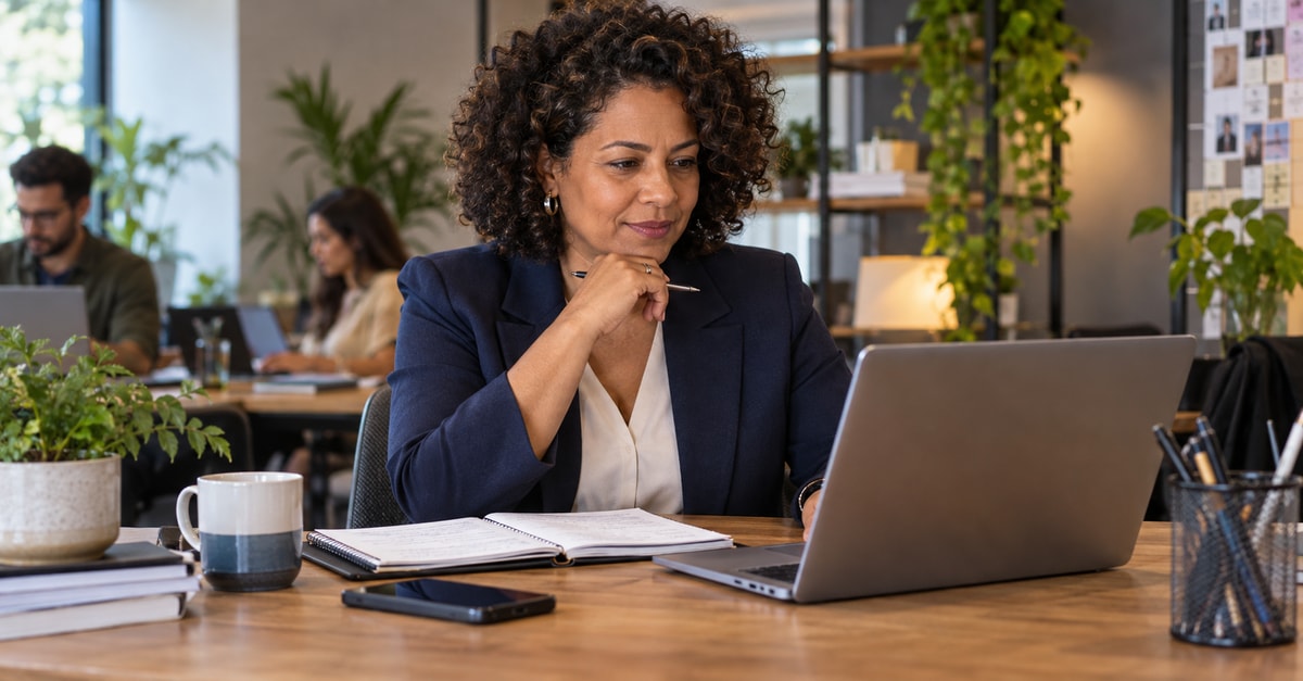 Consultora lê informações no notebook com um caderno de anotações à mesa.