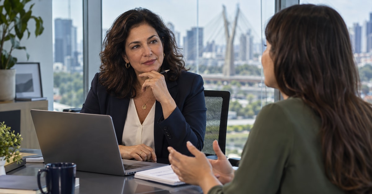 Consultora escuta uma profissional em atendimento individual ao lado de um notebook.